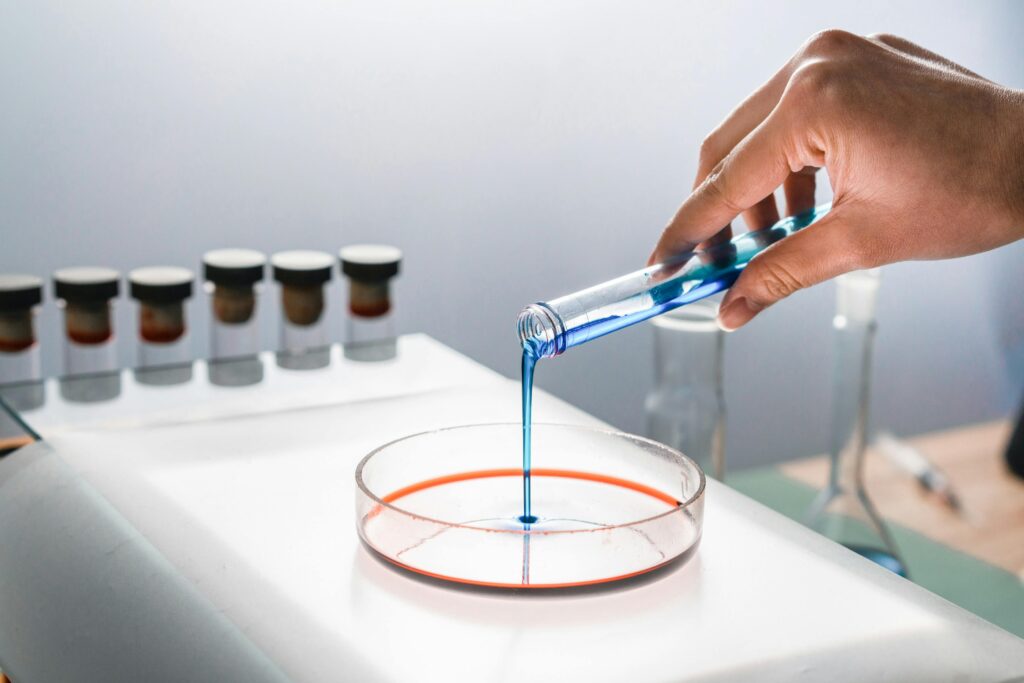 Scientist pouring blue liquid into a petri dish in a laboratory setting, focusing on research and experimentation.