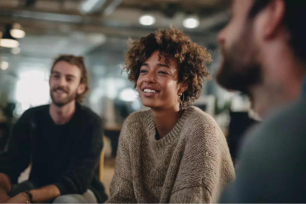 Diverse group of adults in a bright, modern therapy room participating in supportive counseling at a Massachusetts recovery center.