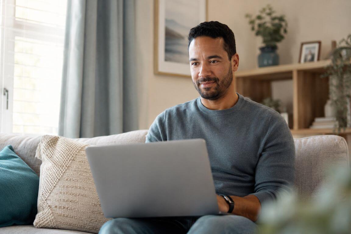 Adult sitting on a couch at home in Massachusetts attending a virtual addiction treatment session on a laptop